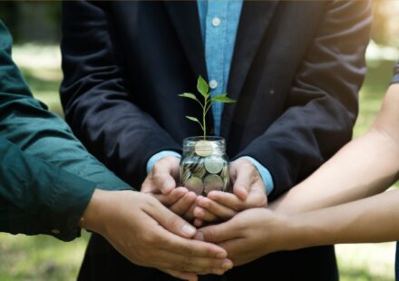 People holding container of coins with a plant growing from it
