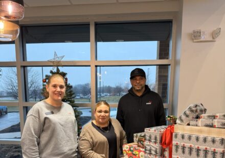Opportunity house & DFCU team members stand in front of cart loaded with gifts.
