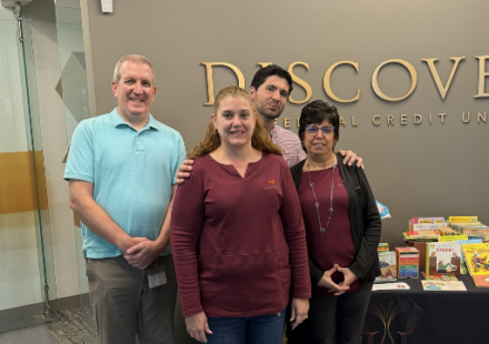 Four people pose together in a lobby beside a brochure table, smiling in front of a Discover sign.